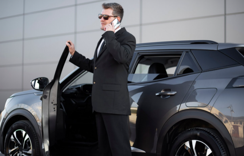 Professional chauffeur standing beside an open car door 