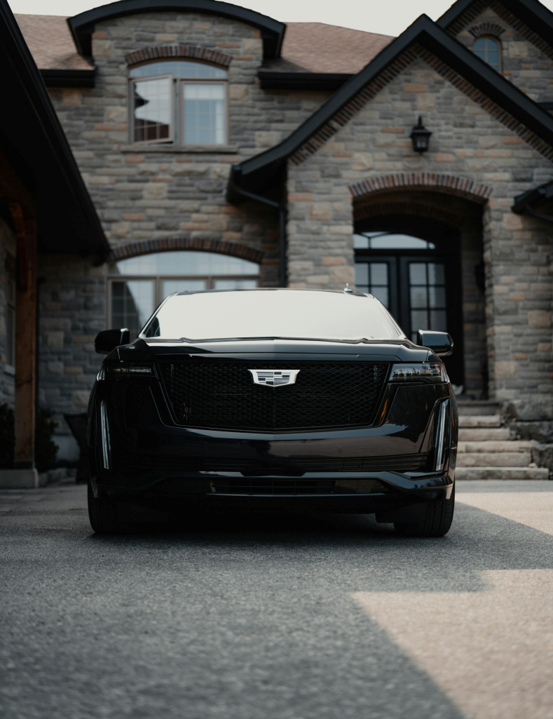 A black Cadillac Escalade parked in front of a house 