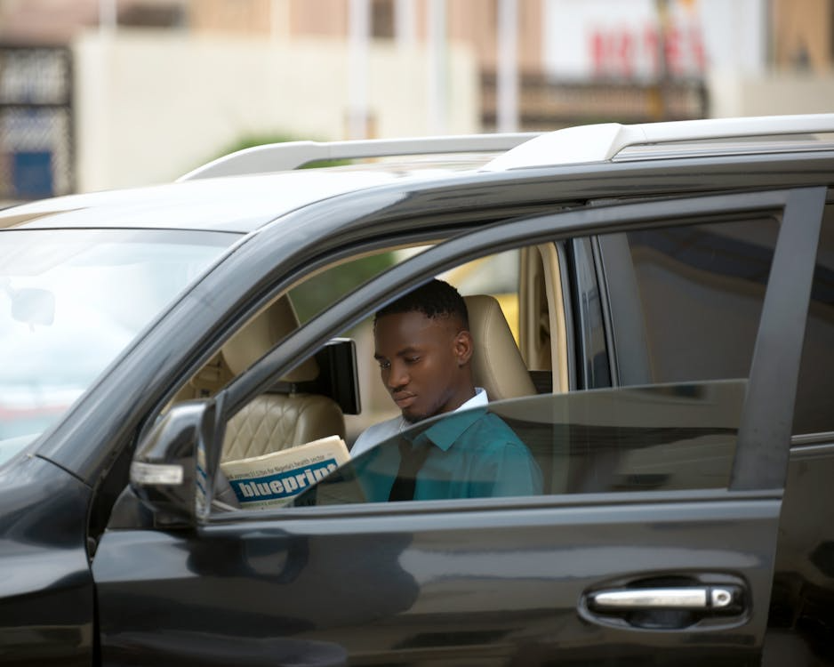 Professional chauffeur reading a newspaper while waiting outdoors for a family pickup
